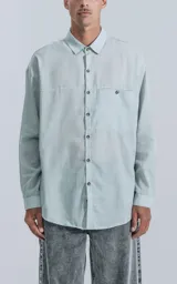 Camisa manga larga verde agua con bolsillo en el pecho, de calce oversize confeccionada en textil plano fresco y liviano.