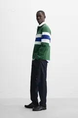 Polo de rugby verde con rayas horizontales azules y blancas, cuello blanco con solapa y cierre de botones, y mangas largas con puños acanalados.