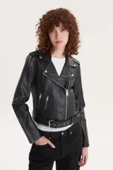 Campera biker negra de cuero sintético con cuello solapa, cierre cruzado con cremallera, bolsillos con cremallera y cinturón ajustable.