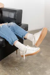 Zapatillas bajas color marfil con detalles dorados en el talón y ojales metálicos. Suela de goma color caramelo y cordones beige.