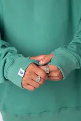 Buzo canguro gris claro de corte oversize, con capucha y cordones negros con letras blancas. Presenta un bolsillo tipo canguro y un estampado pequeño en el pecho y otro en la manga.