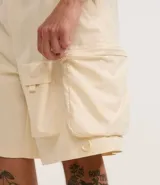 Bermuda color crema de poliéster, corte baggy cropped, con cintura elástica ajustable con cordón y bolsillos cargo funcionales.
