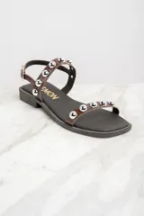 Sandalias bajas de cuero color marrón con apliques de tachas metálicas plateadas.
