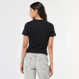 Camiseta negra de punto de canalé fino, con cuello redondo y mangas cortas. Presenta una costura vertical central en el frente que se abre en el ruedo.