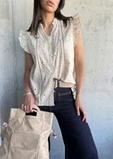 Blusa color beige con bordado calado, cuello mao con volados, mangas cortas con volados y cierre frontal con botones.