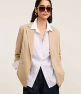 Blazer regular de sastrería color beige, con cuello solapa, sin botón, con bolsillos y detalle de pliegues en las mangas.