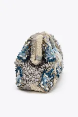 Bolso de mano tipo clutch con cuerpo cubierto de abalorios en tonos beige, azul y gris. Tiene un diseño floral y un cierre imantado. Incluye correa metálica extraíble y bolsillo interior con cremallera.