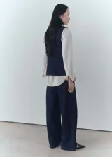 Chaleco de denim azul oscuro con cuello en pico, sin mangas, dos bolsillos delanteros y cierre con botones.