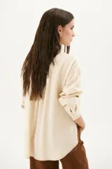 Camisa beige de corte recto, con cuello clásico, cierre frontal con botones, bolsillo en el pecho y mangas largas con puños abotonados.