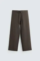 Pantalón marrón de corte ancho, con cintura ajustable con cordón, bolsillos delanteros y traseros tipo parche, detalle de costuras verticales en el frente y cierre frontal con cremallera y gancho metálico oculto.