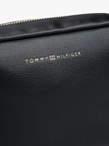 Cartera tipo cámara cruzada (crossbody) color negro, con acabado liso y logo metalizado de Tommy Hilfiger en el frente. Posee un compartimento principal con cierre de cremallera y un asa tejida ajustable.