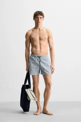 Bañador de hombre con rayas verticales azules y blancas, de corte medio, con cintura elástica ajustable con cordón, bolsillos laterales y trasero con solapa.