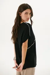 Remera negra de corte holgado con cuello redondo y mangas cortas con dobladillo. Presenta una línea diagonal blanca que cruza el frente desde el hombro hasta la cadera.