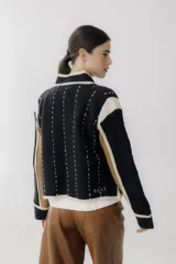 Chaqueta corta de lana color negro con detalles en beige y marrón. Tiene cuello mao, cierre frontal con botones y bolsillos de parche.