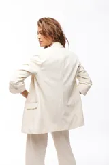 Blazer color crema con solapas de muesca, corte recto, bolsillos delanteros con solapa y mangas 3/4 con botón.