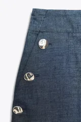 Pantalón ancho azul de tiro alto confeccionado en lino, con bolsillos delanteros con falsos botones y cierre lateral con cremallera oculta.