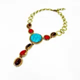 Collar corbatero de bronce con piedras naturales engarzadas. El diseño central presenta una piedra turquesa ovalada, flanqueada por piedras rojas y piedras ojo de tigre ovaladas. De esta piedra central cuelga una cascada de piedras rojas y ojo de tigre engarzadas en marcos de bronce.