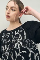 Vestido corto blanco de algodón con bordado floral en relieve, escote redondo con abotonadura frontal y mangas amplias.