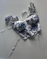 Corset blanco con estampado floral azul, con copas preformadas, tirantes con volantes y lazos ajustables.