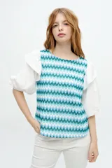 Blusa blanca con mangas abullonadas y volados en las sisas. El cuerpo de la blusa es de tela bordada con pequeños orificios.