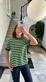 Remera verde con rayas horizontales blancas, cuello redondo y mangas cortas con puños.