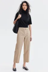 Pantalón cigarette tobillero color beige, con cintura estándar, cierre y pretina prolongada con corchete oculto. Piernas ajustadas con abertura corta en los bajos, bolsillos al bies y bolsillo de atrás decorativo. Pliegues adelante y atrás.