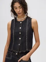 Chaleco corto de denim negro con apliques metálicos y flecos en el ruedo.