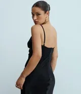 Vestido largo negro de satén con escote pronunciado en V y detalle de recorte central en el busto. Posee breteles finos ajustables y silueta alargada con leve cola en el ruedo.