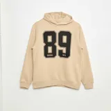 Buzo color beige con capucha y estampado frontal del número 89 en negro con borde blanco.