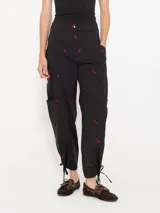 Pantalón cargo negro de poplin bordado con motivos de chiles rojos, cuatro bolsillos plaque con refuerzo triangular en hilo rojo y jareta en el ruedo para ajustar con lazo.