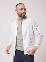 Campera bomber color blanco confeccionada en lino y algodón, con cuello mao, cierre frontal con cremallera, bolsillos frontales con cierre y puños y ruedo acanalados en color beige.