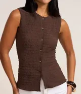 Blusa femenina de corte regular confeccionada en tejido de anarruga texturizado color beige. Presenta cuello redondo, diseño sin mangas y cierre frontal con botones.