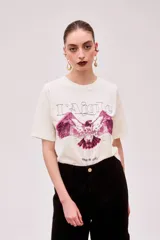 Remera color crudo de corte holgado con estampado de un águila en color fucsia.