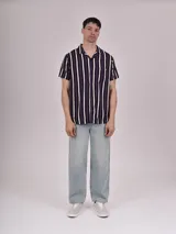 Camisa de manga corta con estampado de hojas color verde sobre fondo beige, cuello solapa y bolsillo en el pecho.