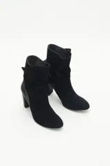 Botas de caña media de gamuza negra, con taco cuadrado y punta fina. Presenta tiras terminadas con borlas que se cruzan y atan alrededor de la caña.