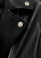 Chaqueta de cuero ovino negra, estilo biker, con cuello con solapa, cierre frontal asimétrico con cremallera, mangas largas con cremallera en los puños, dos bolsillos laterales con cremallera y forro interior de poliéster.