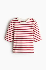 Remera entallada de punto a rayas rojas y blancas con cuello redondo y mangas cortas con botones dorados en los hombros.