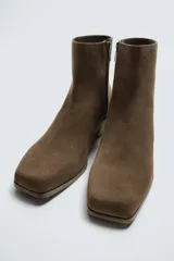 Botín de cuero negro con acabado serraje, cierre de cremallera lateral, horma cuadrada y tacón de 5 cm.