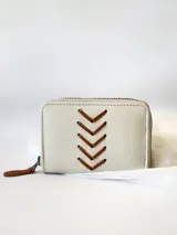 Billetera pequeña de cuero color crudo con cierre metálico y monedero interno. Presenta costuras decorativas en forma de espiga.