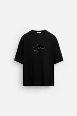 Camiseta negra de corte holgado, con cuello redondo y mangas cortas. Estampado frontal con diseño abstracto en color blanco.