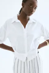 Camisa blanca de lino y viscosa, de corte holgado, con cuello clásico, botones frontales, mangas cortas y bajo redondeado.