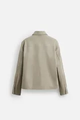 Sobrecamisa color arena de corte recto, con cuello solapa, cierre frontal con cremallera, manga larga con puños abotonados, dos bolsillos de plastrón con solapa en el pecho y dos bolsillos laterales en la costura de la cadera.