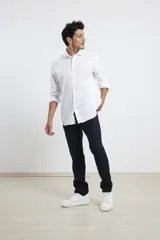 Camisa blanca de algodón premium, corte clásico, cuello inglés, cartera abotonada, mangas largas con puños ajustables y bajo redondeado.