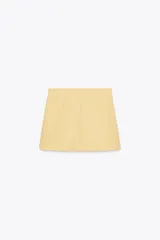 Minifalda color amarillo pálido de tiro alto con cinturón del mismo tejido y hebillas metálicas. Cierre trasero con cremallera oculta.