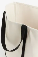Bolso de playa de lona color crudo con asas de cinta negra.