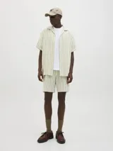 Camisa de manga corta a rayas verticales color crudo y verde, con cuello resort, corte holgado y cierre frontal con botones.