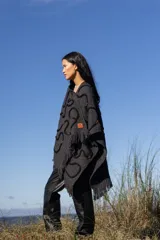 Ruana negra con diseño de líneas curvas en relieve y flecos en el borde inferior.