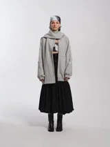 Buzo hoodie oversize de felpa de algodón color gris, con capucha y bufanda integrada que envuelve el cuello. Presenta cierre frontal y bolsillos canguro.