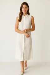 Vestido midi color crema, de lino, corte ancho, sin mangas, con cuello camisero y abotonadura frontal.