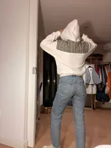 Canguro blanco con capucha y diseño a cuadros en la parte superior y bolsillo frontal.